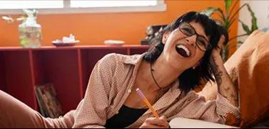 Mulher sorrindo enquanto olha para algo fora da câmera e escreve em um caderno.