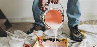 Pintor despejando lata de tinta dentro da bandeja para pintura.