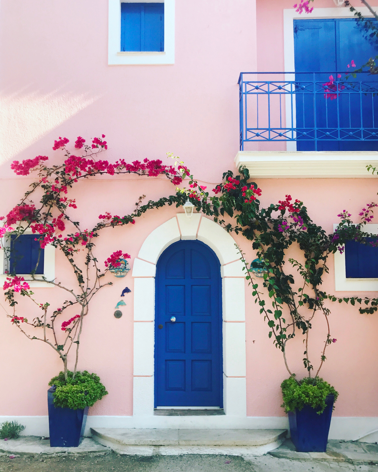 Fachada de casa com janelas e porta azul escuro, com bordas de cor branca e paredes rosa claro.