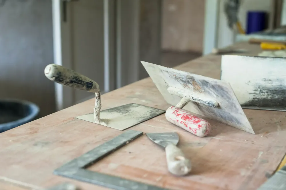 Lixa, espátula, desempenadeiras de aço e régua sobre uma bancada.