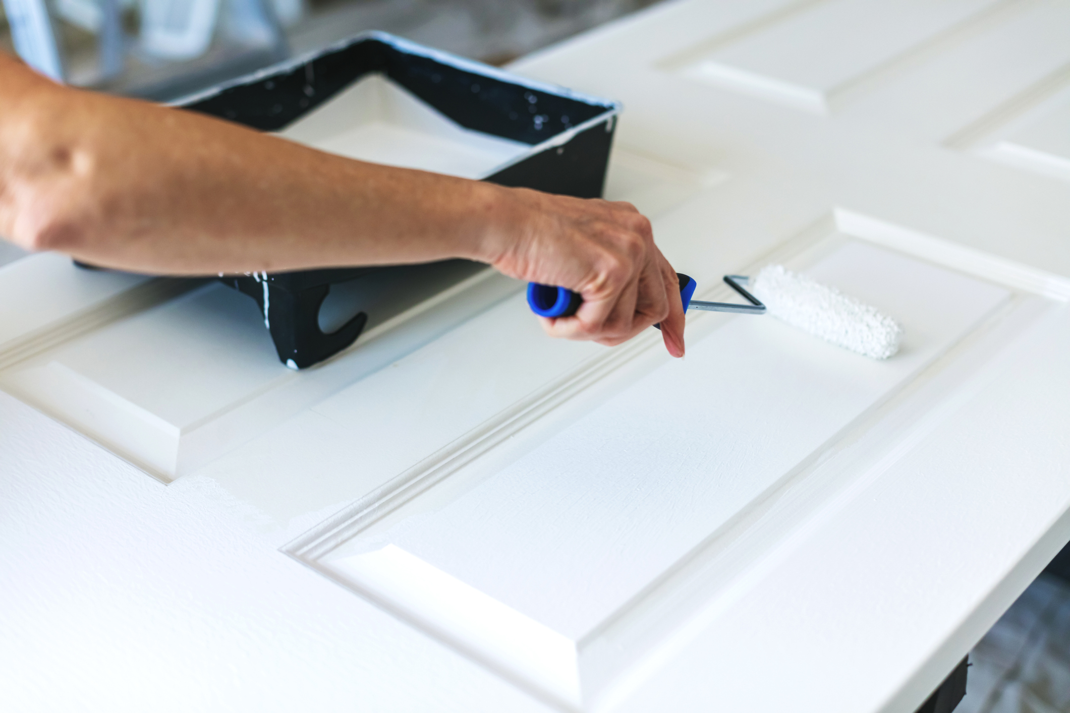 Porta sendo pintada, através do rolo de pintar, com esmalte sintético branco.