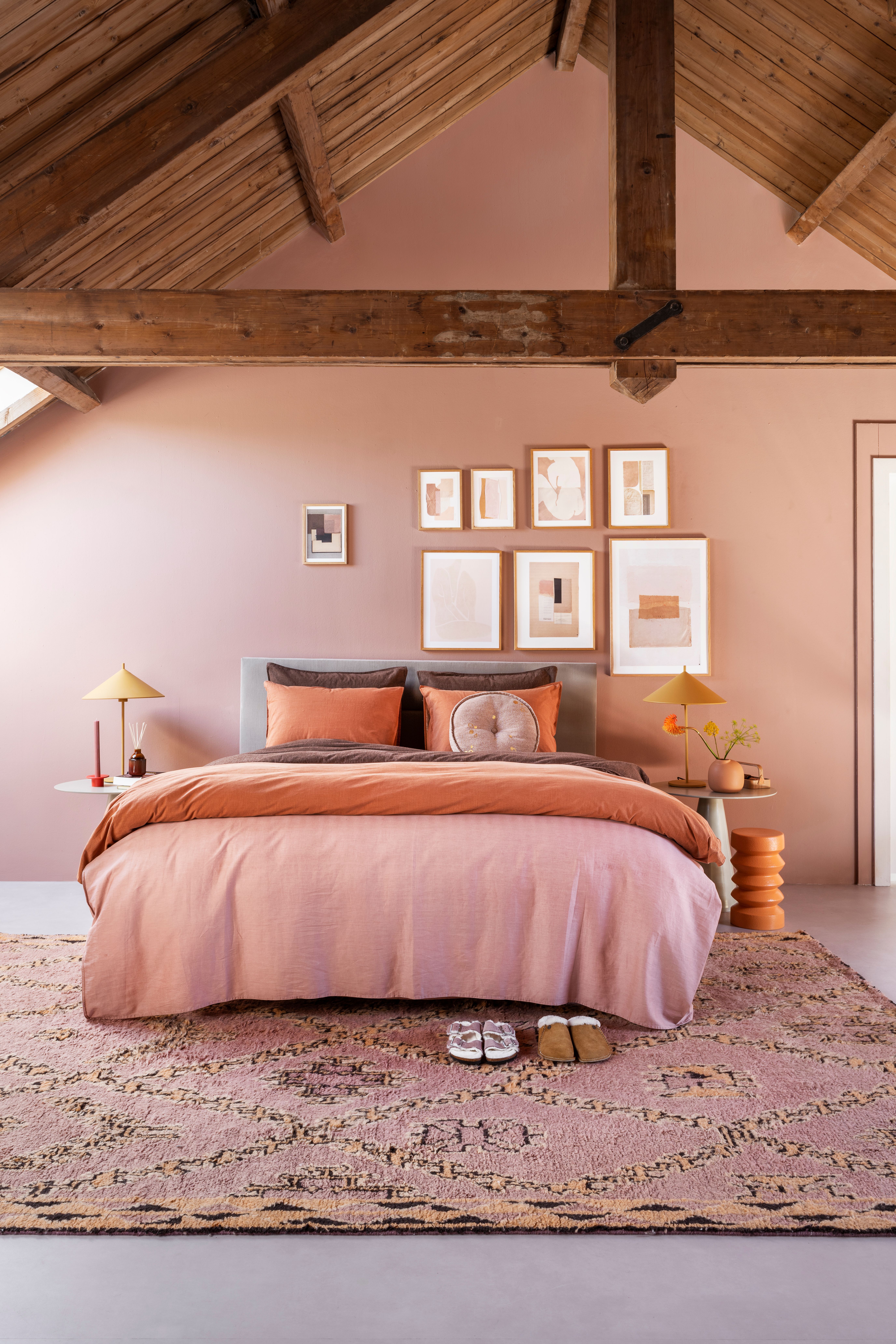 Quarto de casal pintado com rosa chiclete. O teto do quarto é alto, de madeira e forma triangular.