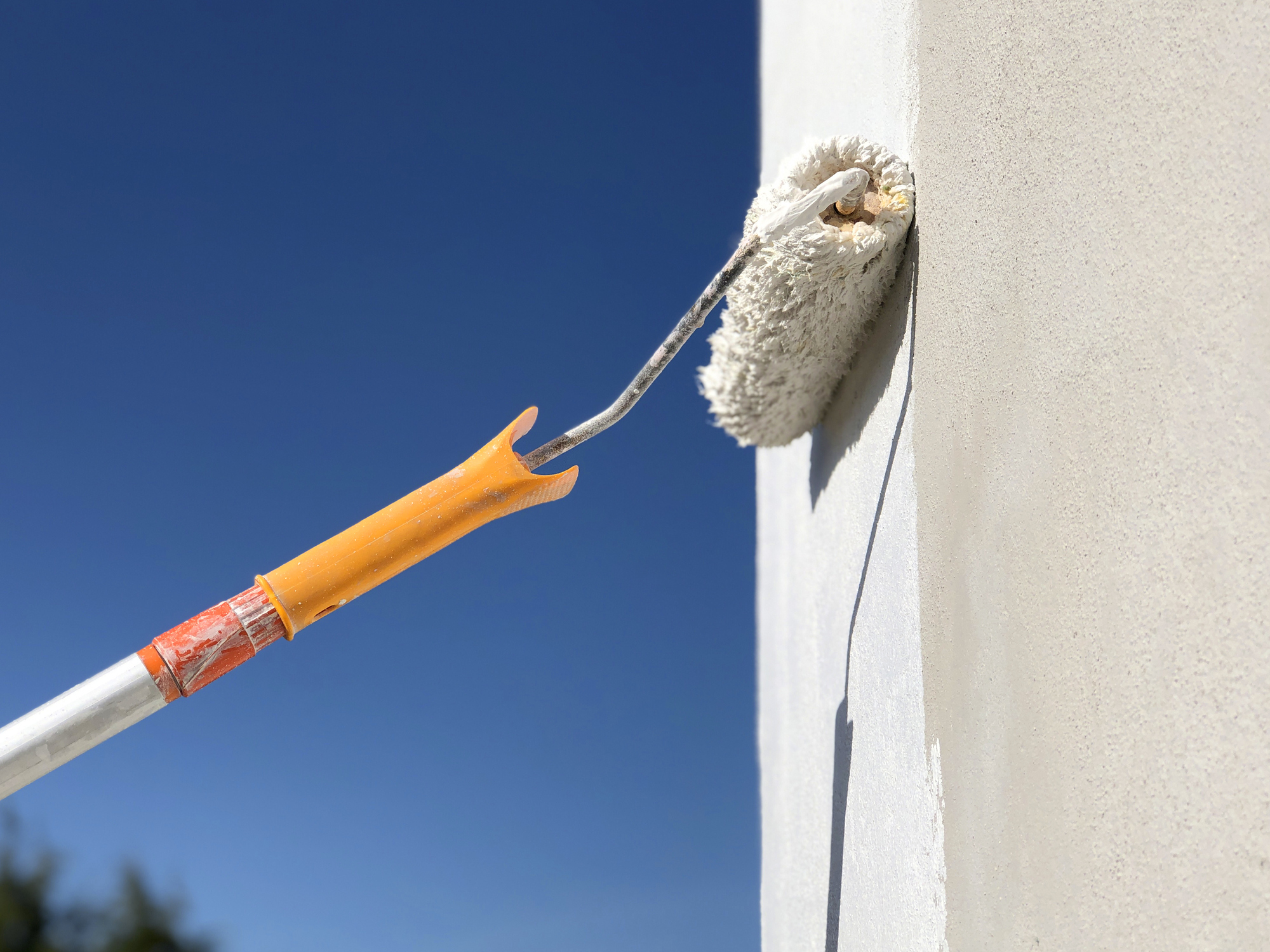 Rolo de pintar com extensor, pintando uma parede de branco.