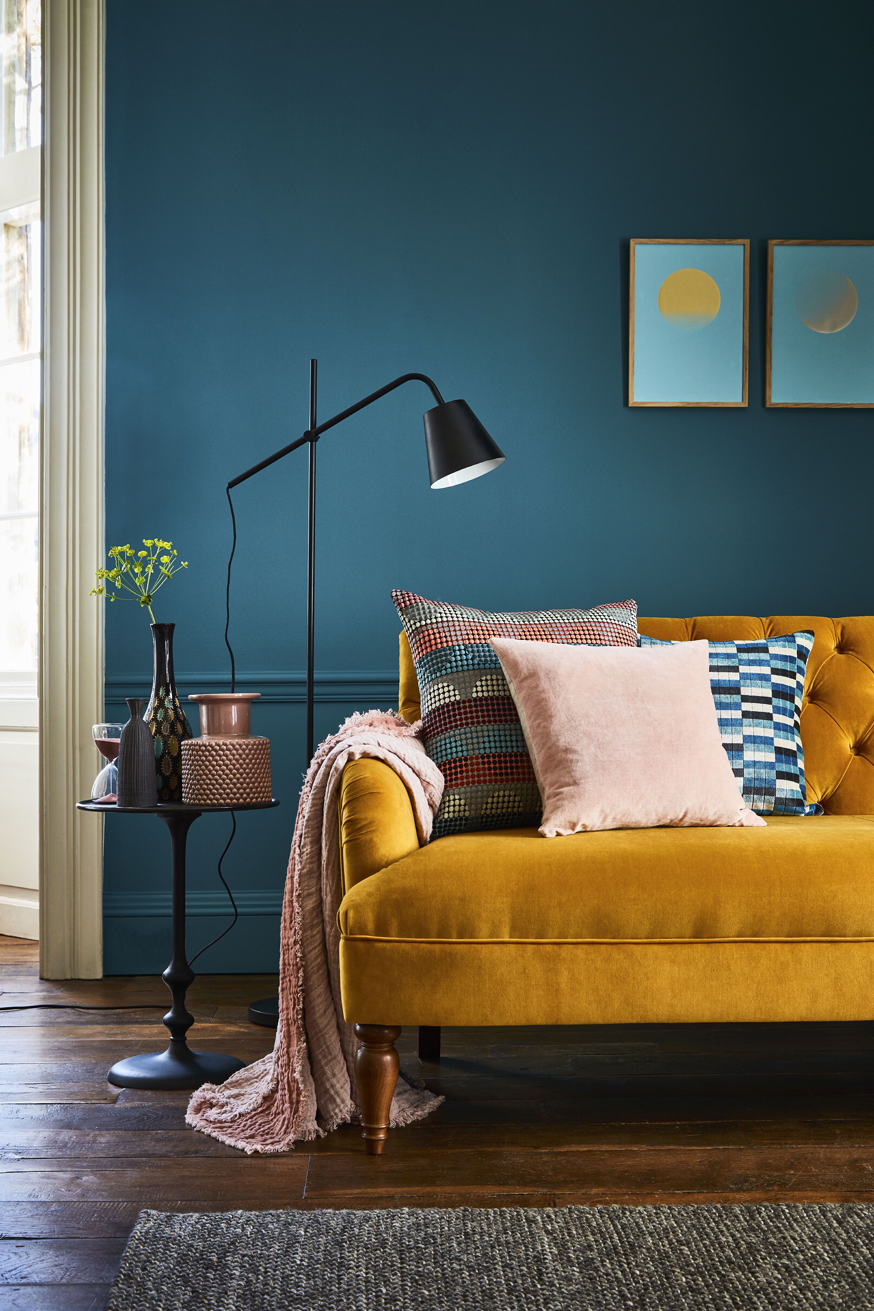 Sala com parede pintada com cor azul intenso. Um sofá amarelo mostarda dá contraste no ambiente.
